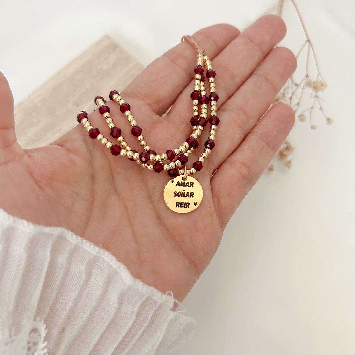 Meaningful gold and burgundy bracelet with an engraved pendant that says “Amar, Soñar y Reír,” designed for everyday wear and adjustable for a comfortable fit.