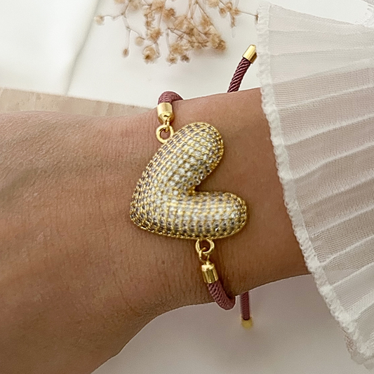 Adjustable bracelet with a sparkling gold-tone heart charm covered in crystal accents, paired with a dusty rose cord and gold-tone hardware.