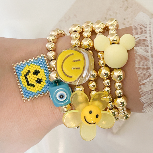 Wrist wearing multiple colorful bracelets with smiley face designs on a light background