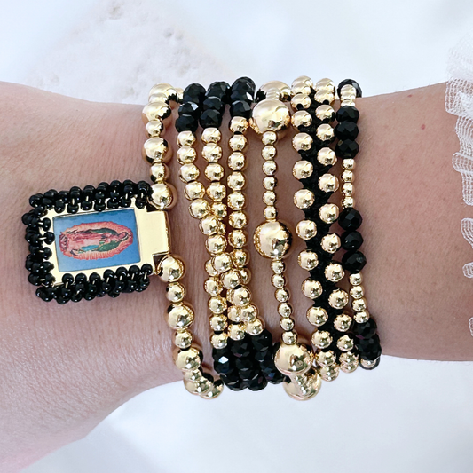 Wrist wearing multiple black and gold beaded bracelets on a light background