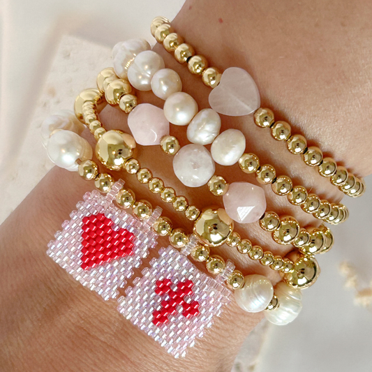 Close-up of a wrist wearing multiple beaded bracelets with heart designs.