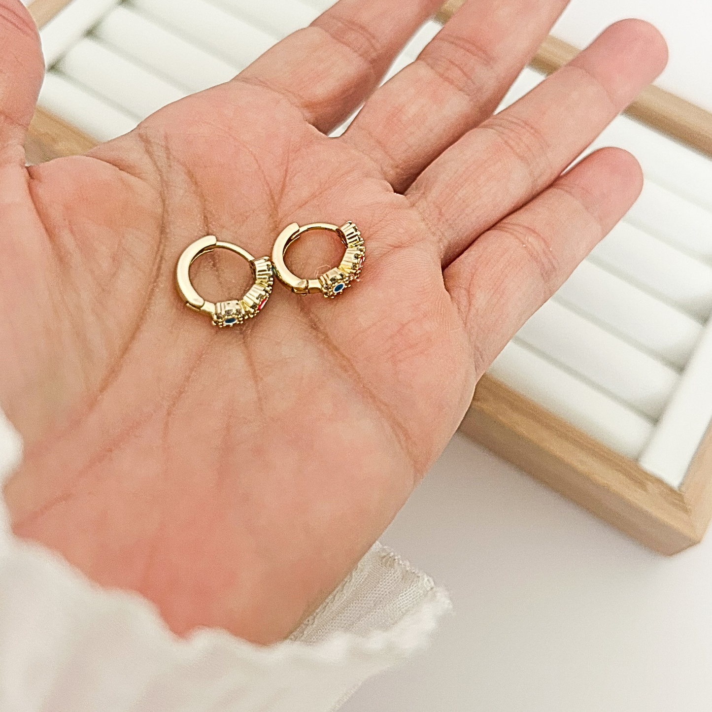 Pair of gold huggie hoop earrings with triple evil eye stones held in open palm