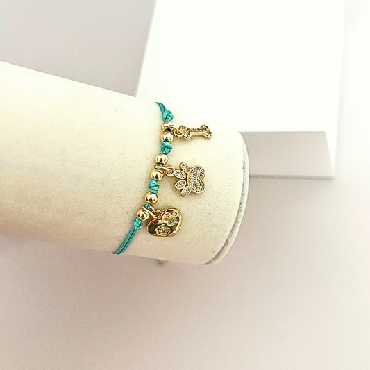 Handmade pet lover bracelet with a turquoise cord, sparkling paw charm, bone charm, and heart accent.