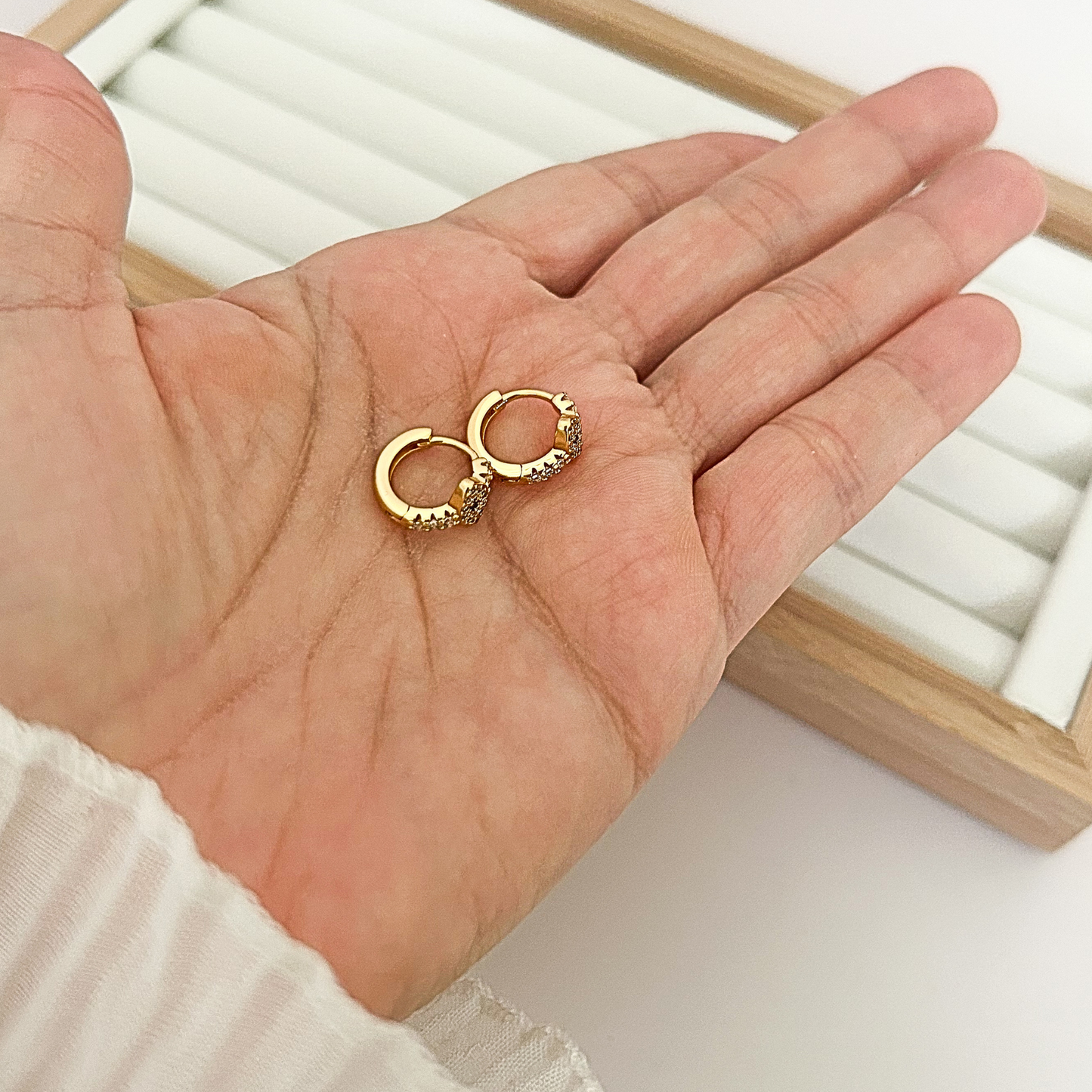 Pair of gold huggie hoop earrings with evil eye charm held in open palm