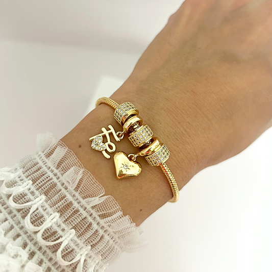 Woman wearing a gold-tone bracelet featuring heart and faith charms with sparkling crystal details.