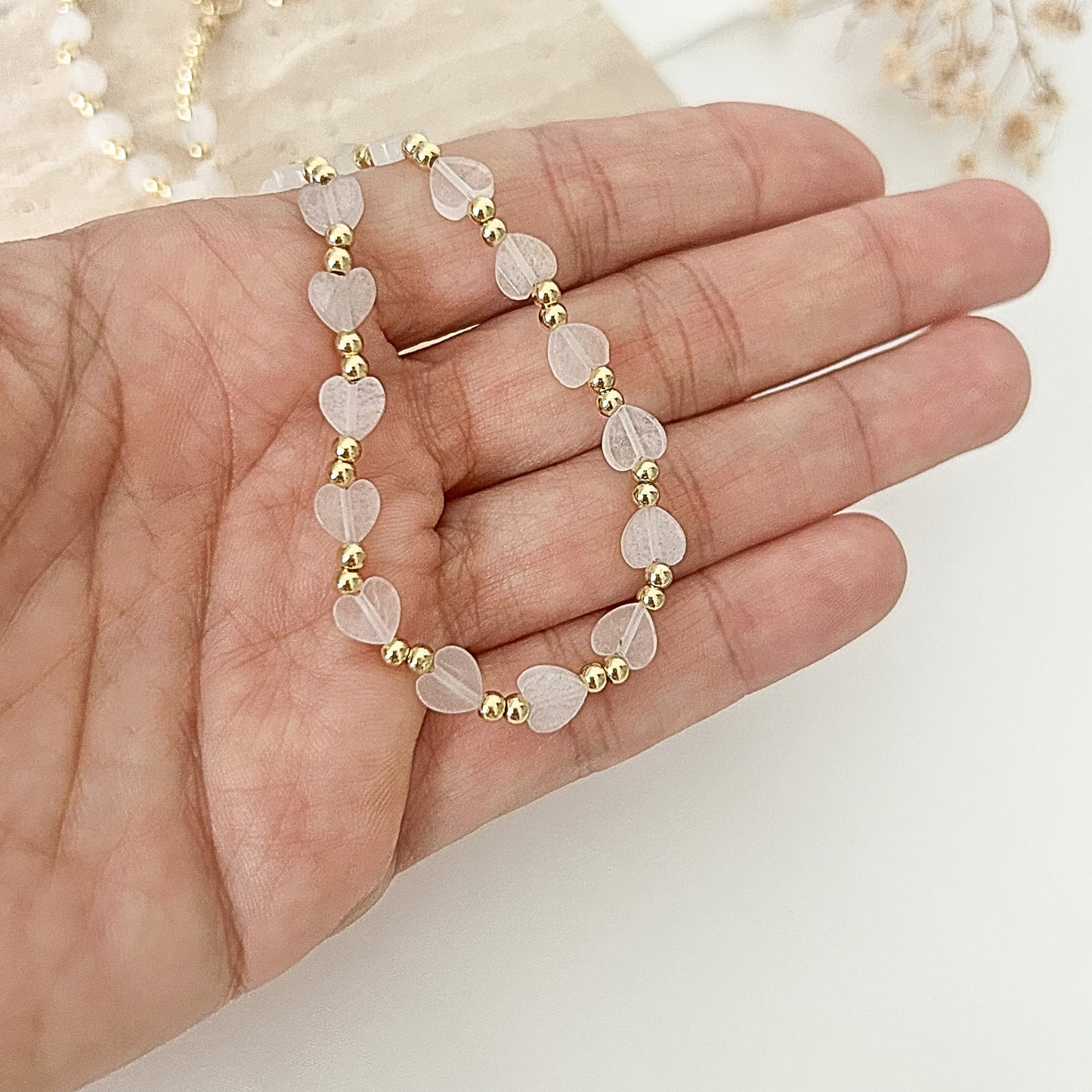 Close-up of a feminine heart bead necklace with translucent frosted hearts and gold-tone accents, shown in hand.