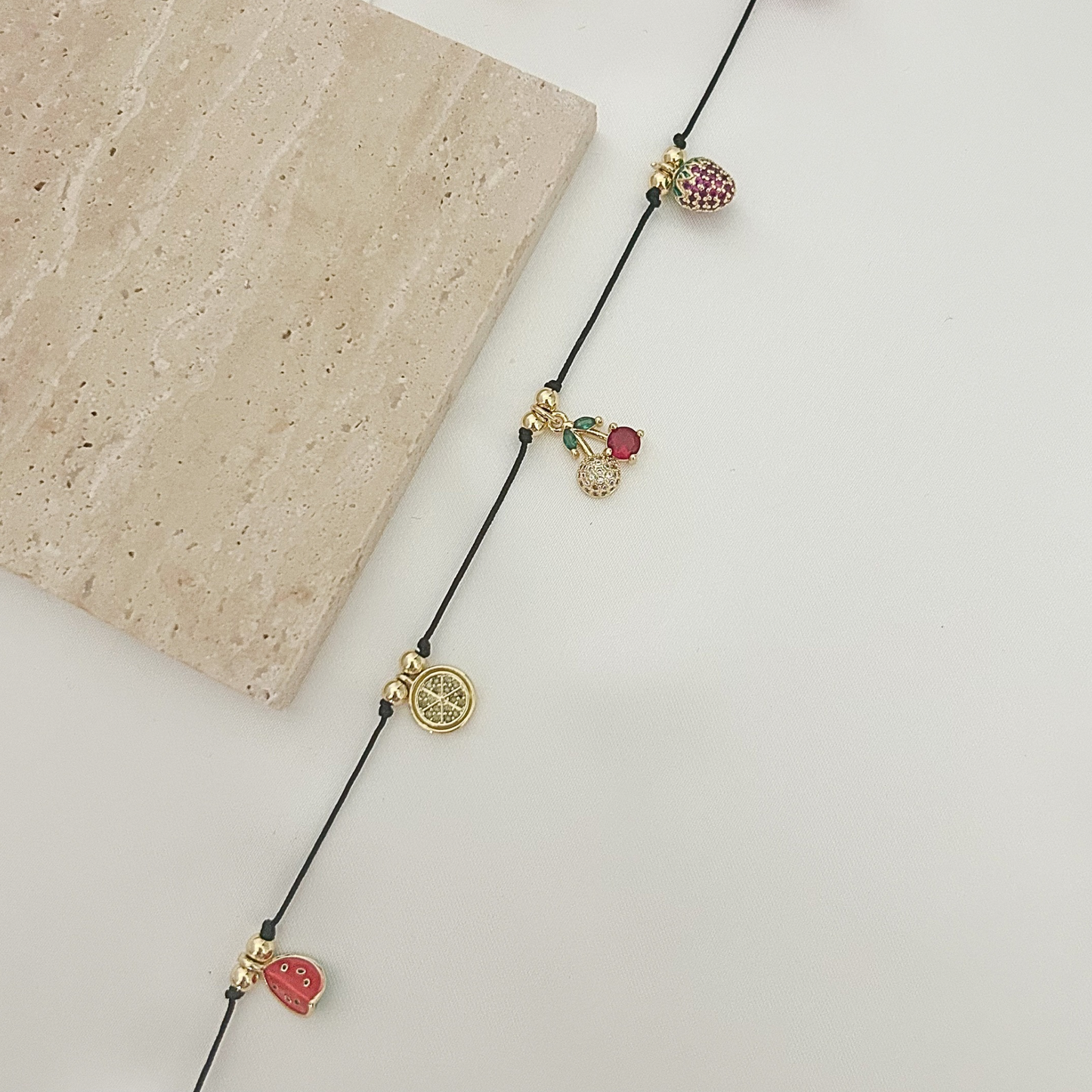 Colorful fruit-themed necklace with gold-tone charms and a black cord, combining playful summer-inspired details with a trendy, lightweight design.