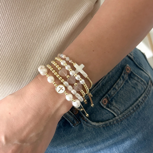 Pink pearl cross bracelet set with gold beads worn on wrist