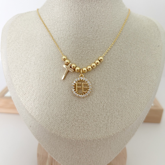 Gold necklace with a cross and 'FE' pendant on a mannequin bust.