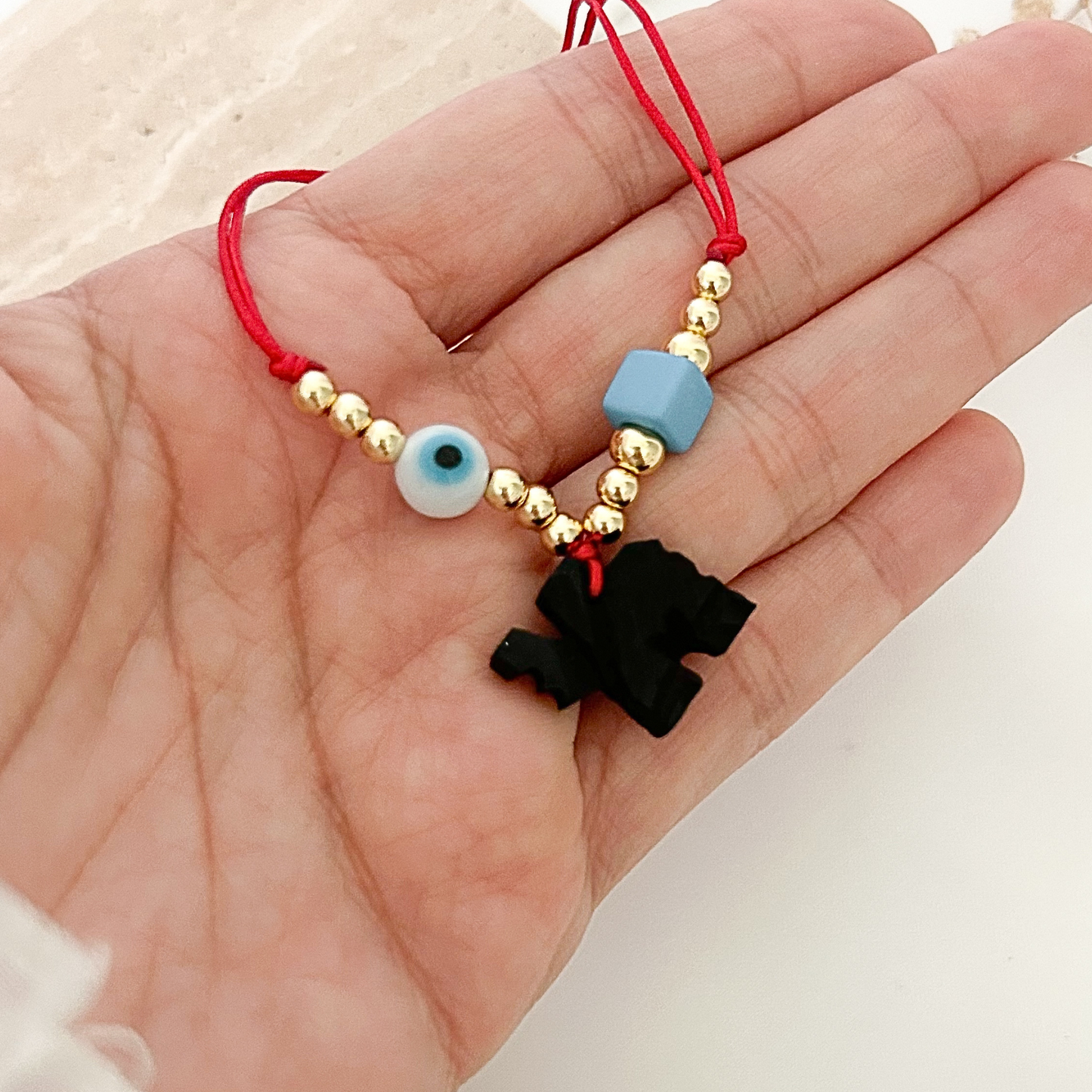 Close-up of an adjustable red bracelet featuring gold-tone beads, a blue evil eye charm, and a black elephant pendant symbolizing protection, wisdom, and good luck.