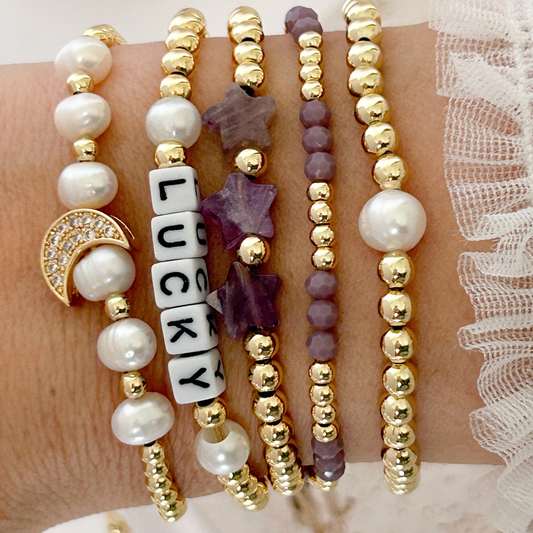 Set of beaded bracelets with a 'Lucky' charm on a wrist against a lace background