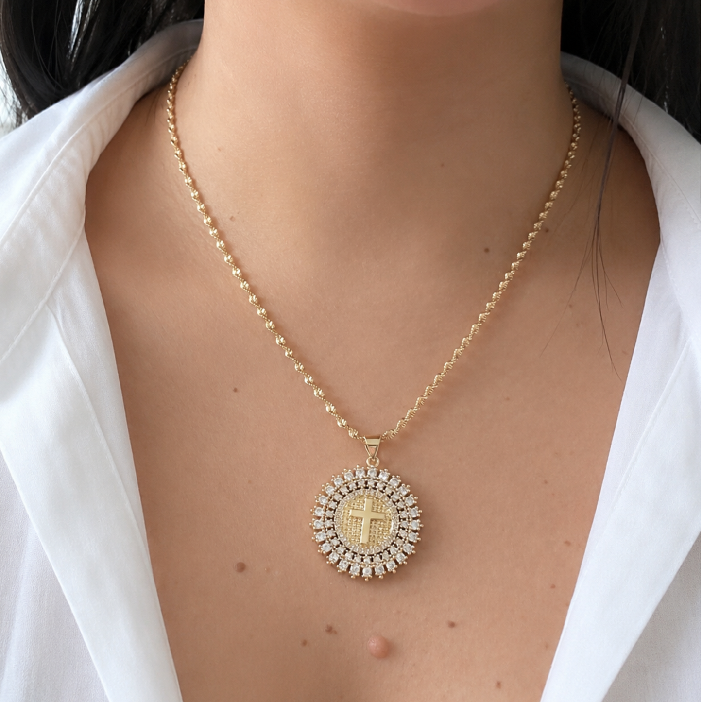 Faith-inspired gold necklace worn with a white blouse, showcasing a radiant crystal halo pendant with a cross design. Perfect for everyday elegance and meaningful gifting.