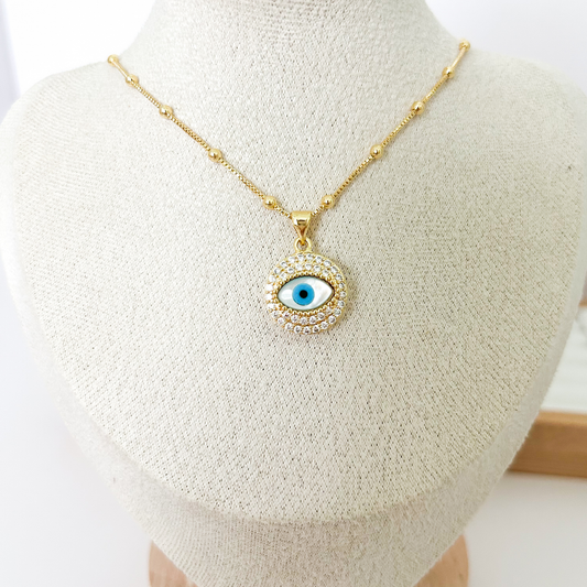 Gold evil eye pendant necklace with blue enamel and zirconia halo on gold chain on white background — Citrika
