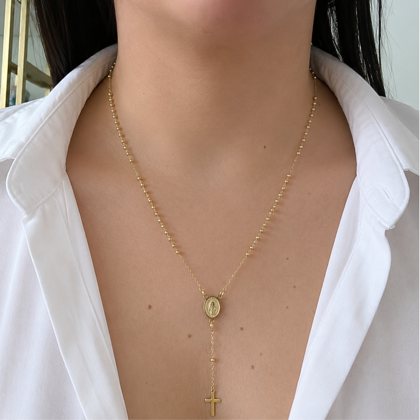 Elegant gold Saint Benedict necklace worn with a white blouse, featuring a dainty cross drop and fine beaded chain for a timeless faith-inspired look.