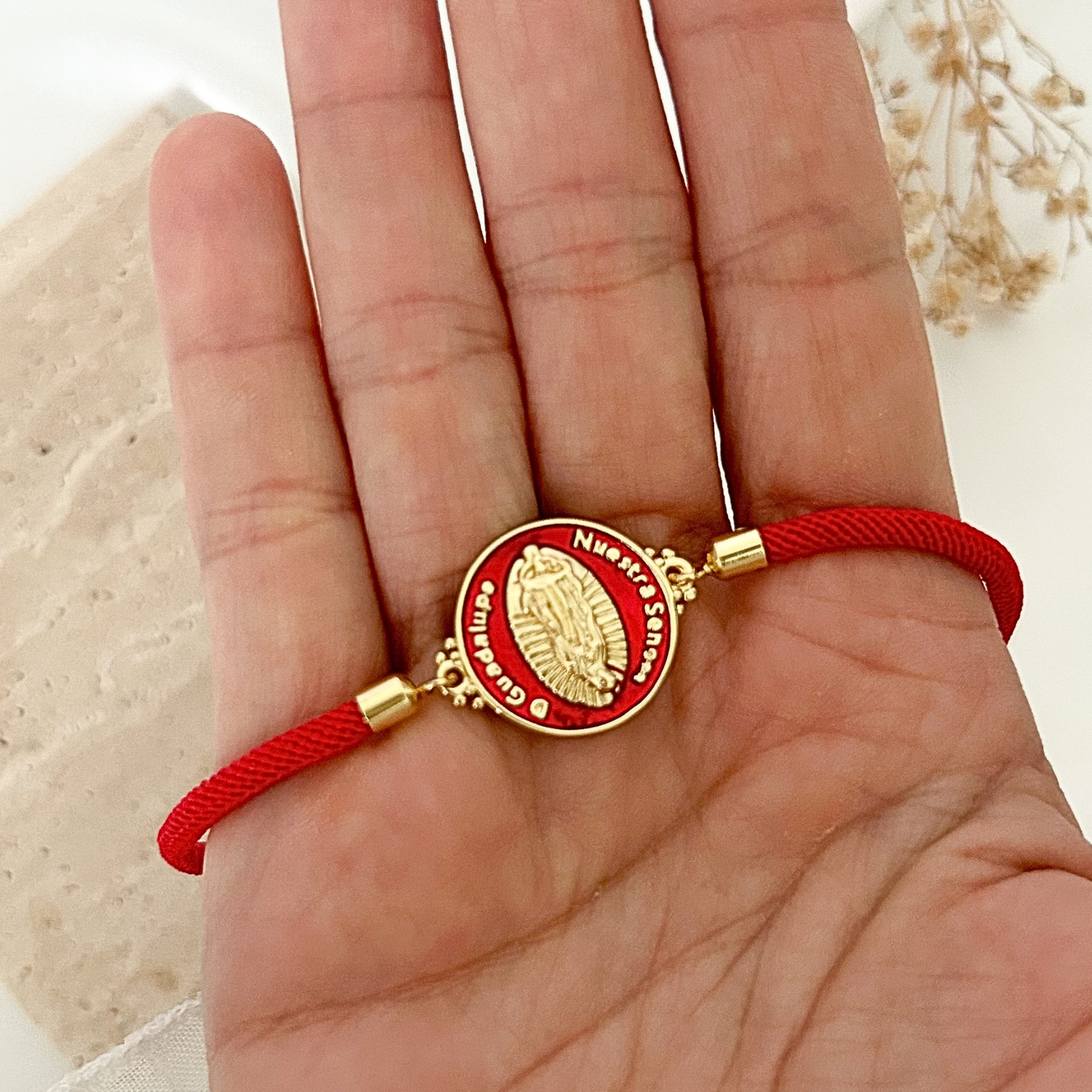 Handheld view of a minimalist devotional bracelet with a red adjustable cord and a detailed Virgen de Guadalupe charm framed in gold and red enamel, perfect for everyday wear or gifting.