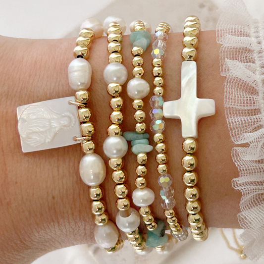 Multiple bracelets with pearls, gold beads, and a cross charm on a wrist.