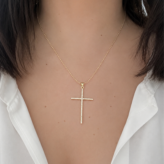 Mujer luciendo un delicado collar dorado con cruz brillante, combinado con una blusa blanca para un estilo sofisticado y atemporal.