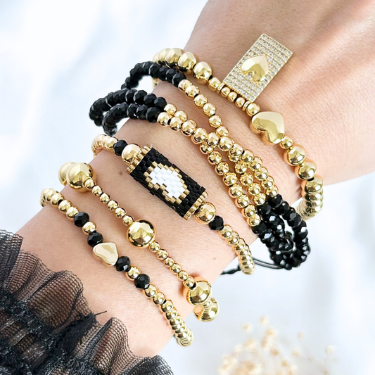 Hand wearing multiple gold and black beaded bracelets on a blurred background