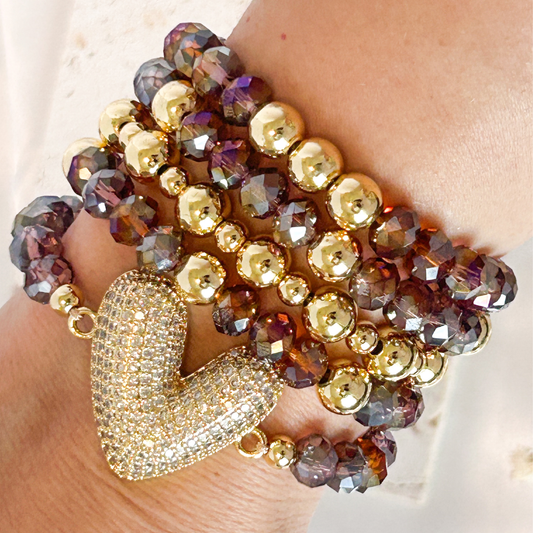 Multistrand beaded bracelet with a gold heart charm on a wrist.