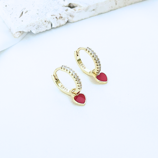 Gold hoop earrings with red heart charms on a white surface