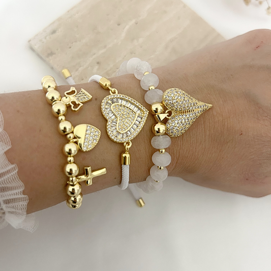 Gold beaded bracelet with cross, heart, and angel charms worn on the wrist
