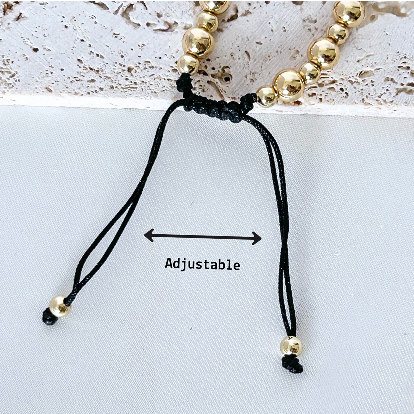 Black adjustable cord bracelet with gold beads on a light gray background