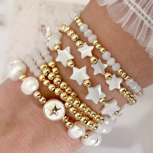 Stack of gold and white beaded bracelets on a hand against a soft background