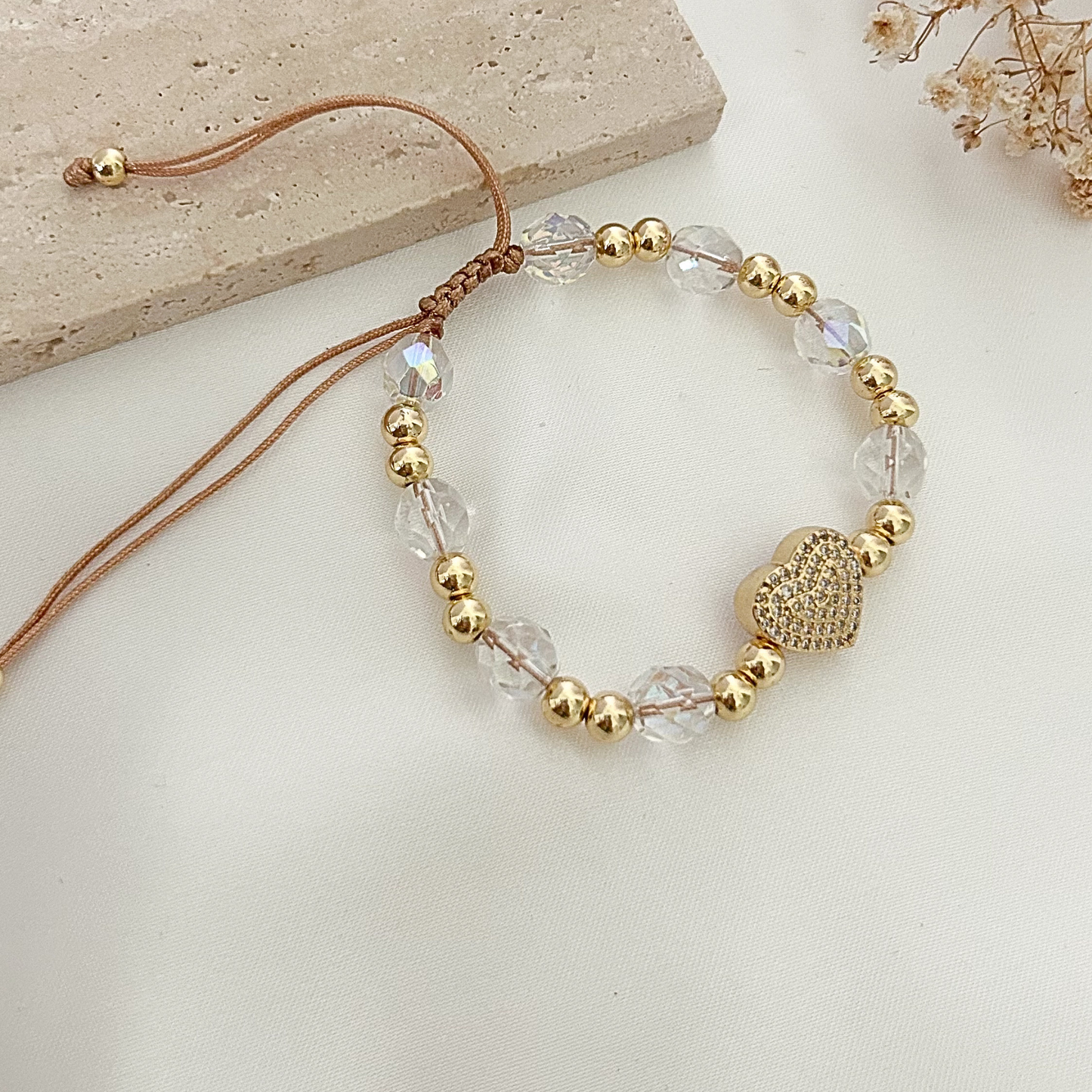Adjustable bracelet with iridescent crystal beads, gold-tone accents, and a pavé heart charm displayed on a neutral fabric background.