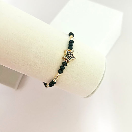 Black beaded bracelet with a sparkling star centerpiece displayed on a jewelry stand, combining black and gold details.