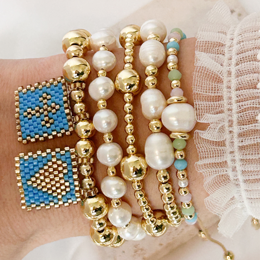 Hand wearing multiple beaded bracelets with gold, pearl, and blue beads.