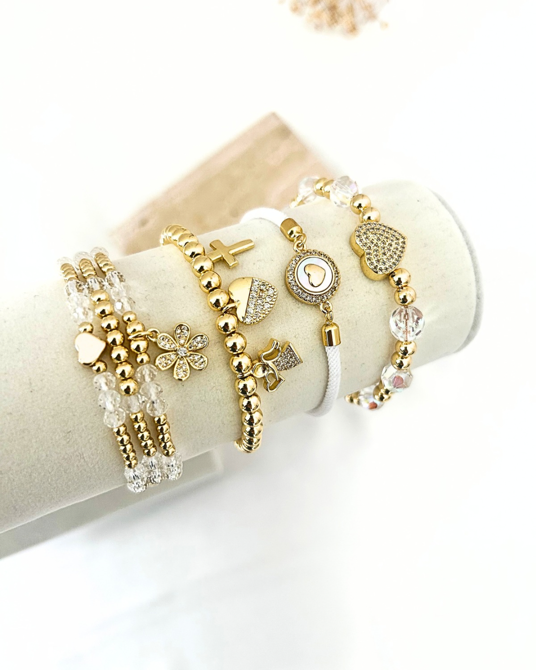 Stack of gold crystal  bracelet with heart, cross, flower and charm details displayed on a jewelry stand.