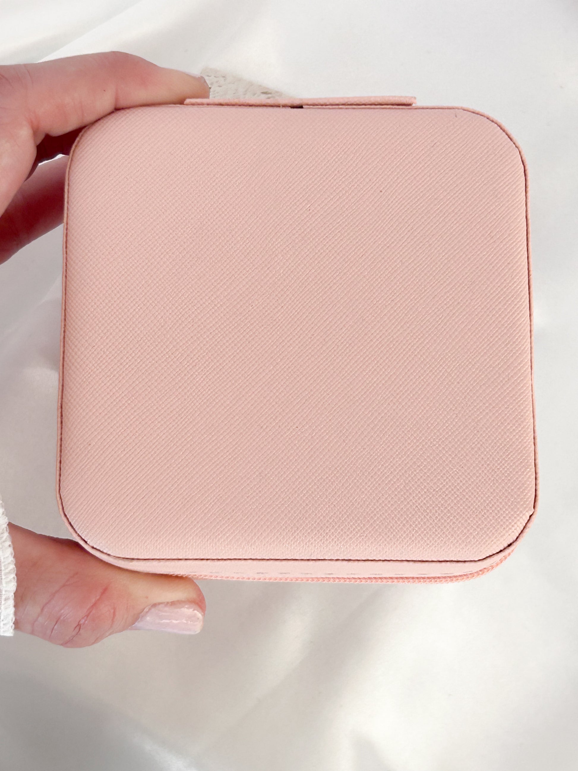Pink jewelry case held by a hand on a white background