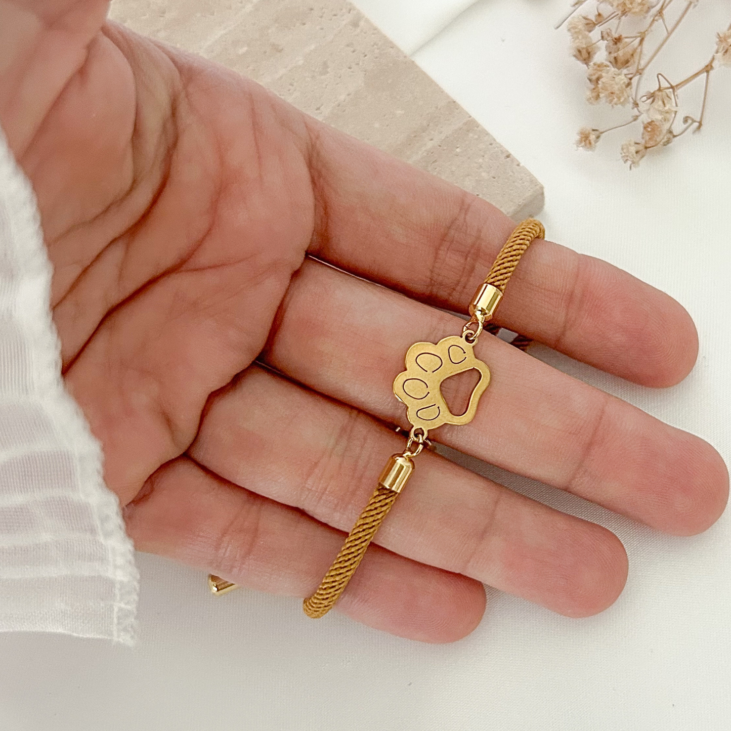 Handheld view of a pet-inspired bracelet with a gold paw charm centerpiece, adjustable sliding closure, and sleek minimalist design, perfect for dog lovers and pet parents.