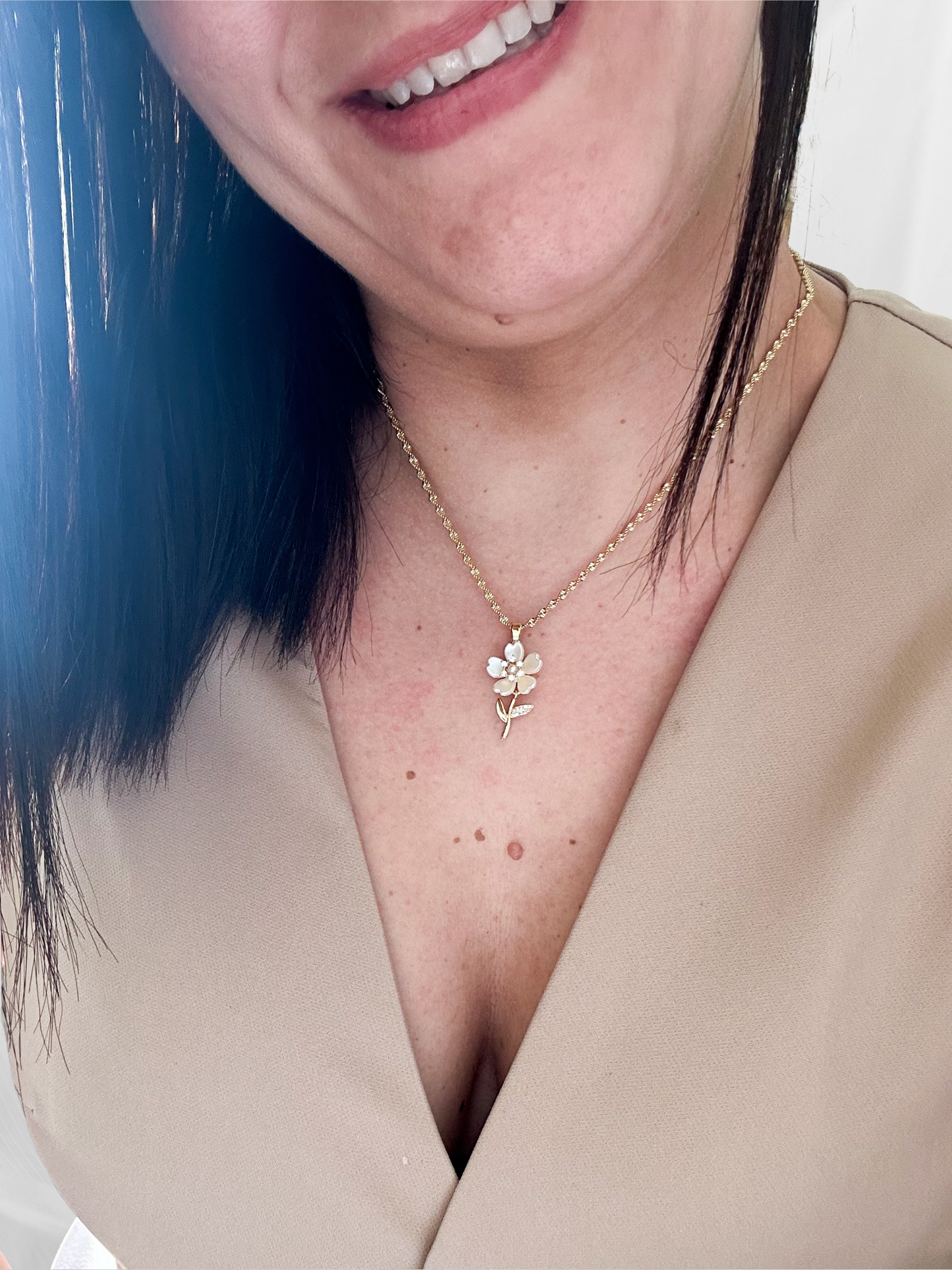 Close-up of a person wearing a gold necklace with a floral pendant.