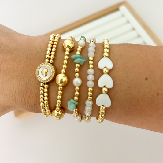Gold bracelet stack with green stones and heart charm styled on wrist