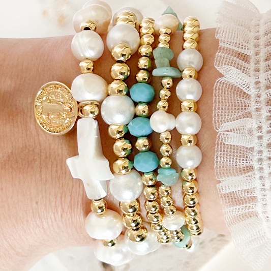 Multiple beaded bracelets with pearls, gold beads, and turquoise stones on a wrist.