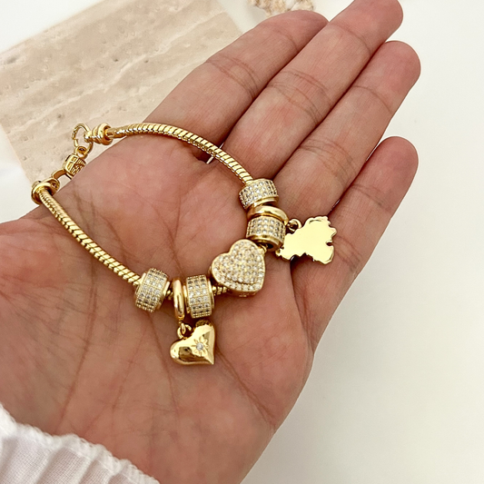 Gold-tone charm bracelet with sparkling pavé accents, featuring heart-shaped charms and a Venezuela map charm, displayed in the palm of a hand.