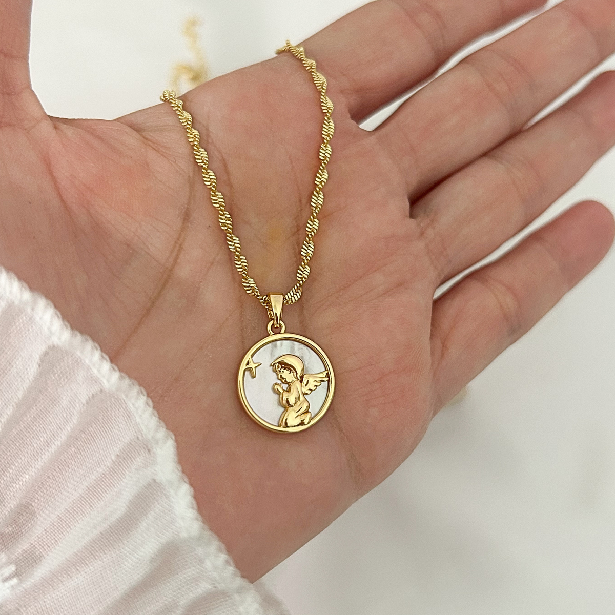 Gold guardian angel pendant necklace with a mother-of-pearl background, shown in hand to highlight its size, elegant details, and textured gold chain.