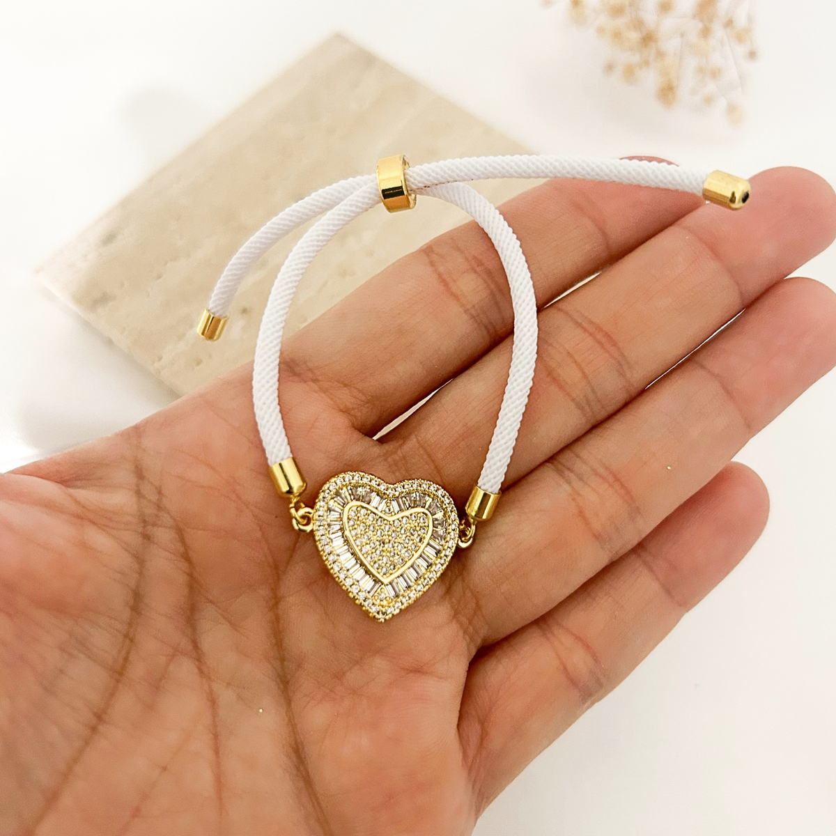 Hand holding white cord heart bracelet to show detail