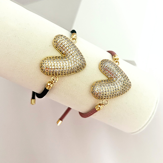 Adjustable heart bracelet available in black and mauve cord variations, featuring a large gold-tone heart charm covered in sparkling crystals.