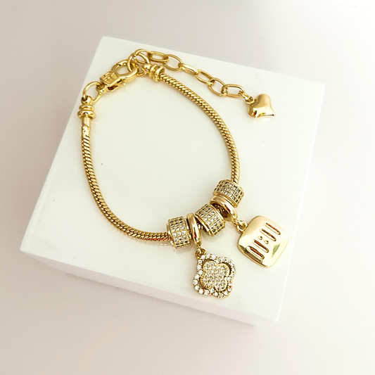 Gold-tone charm bracelet featuring sparkling accents, decorative beads, a quatrefoil pendant, and an engraved 11:11 charm.