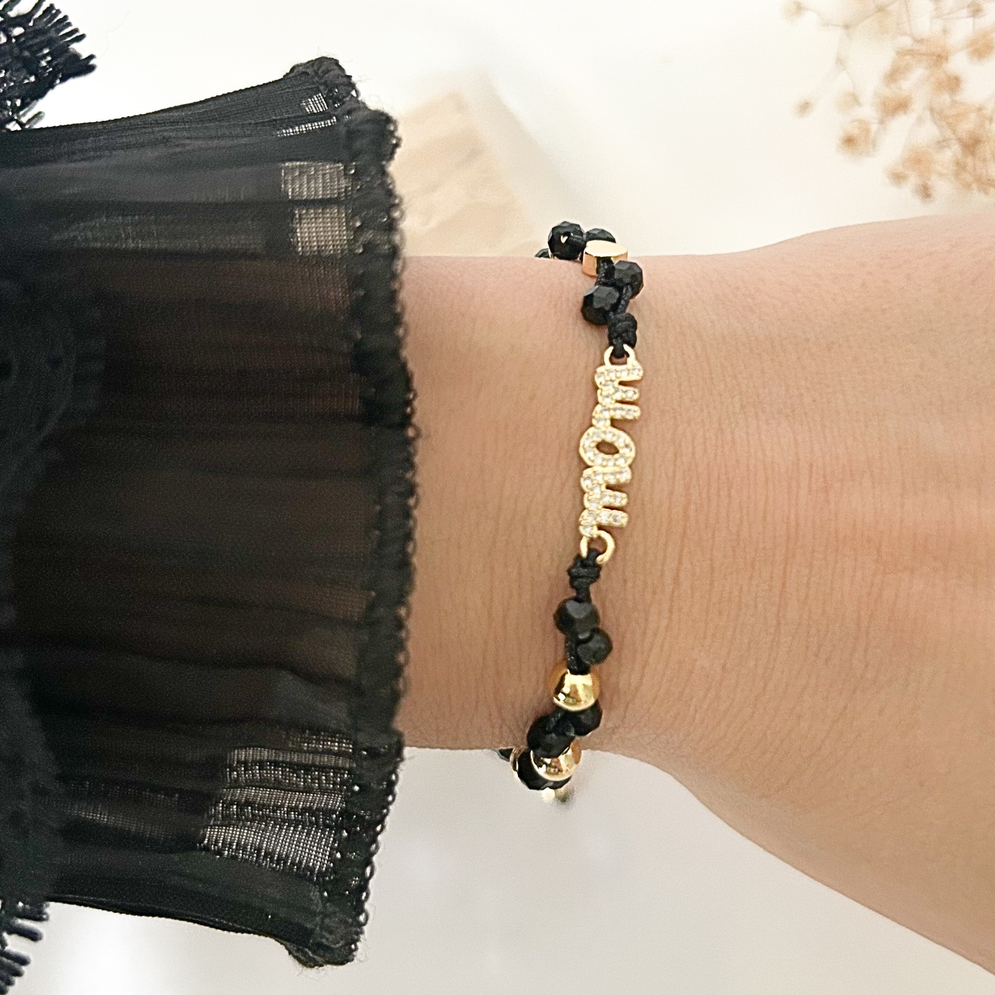 Elegant black crystal bracelet worn on the wrist, showcasing a rhinestone-studded “Mom” charm with gold accents, paired with a sheer black sleeve for a sophisticated and meaningful look.