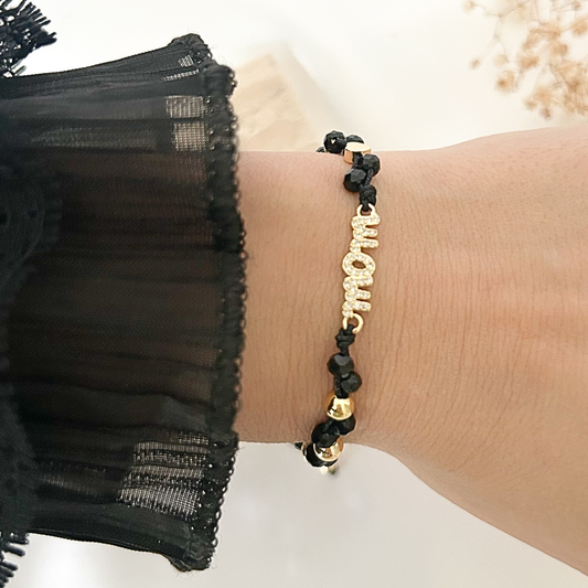 Elegant black crystal bracelet worn on the wrist, showcasing a rhinestone-studded “Mom” charm with gold accents, paired with a sheer black sleeve for a sophisticated and meaningful look.