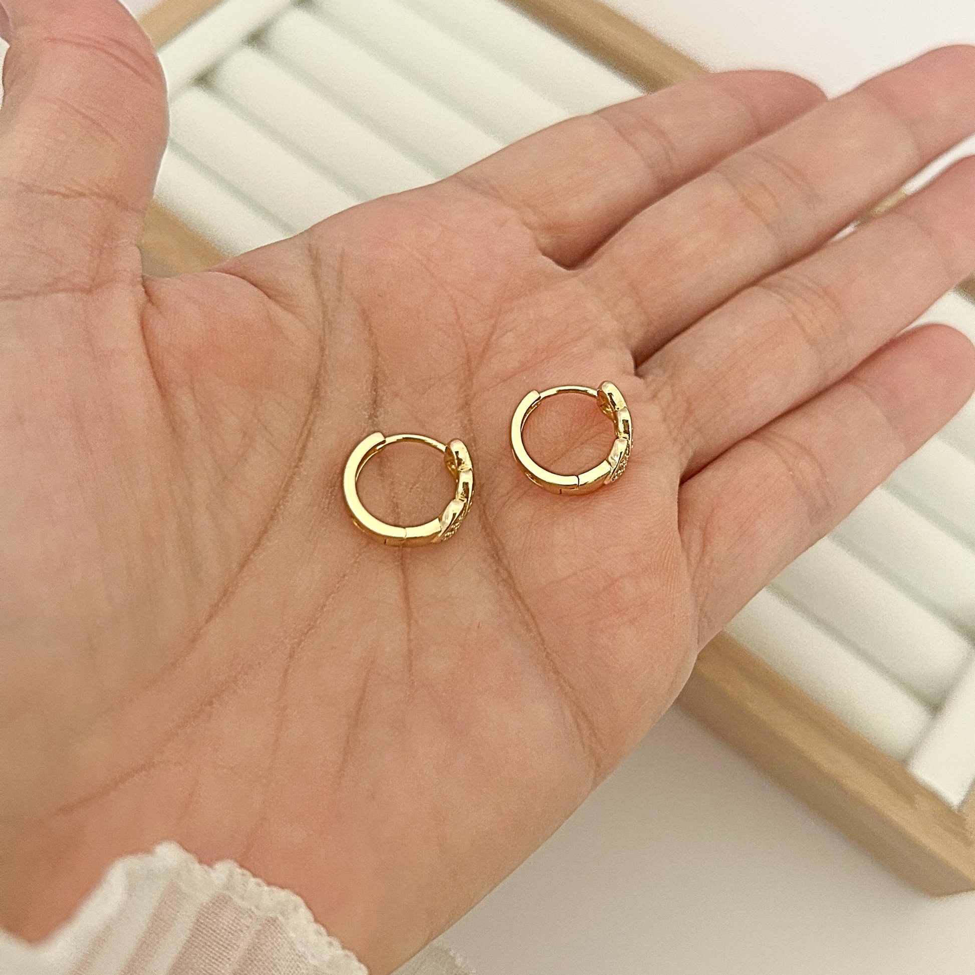 Pair of gold huggie hoop earrings with triple heart charm held in open palm