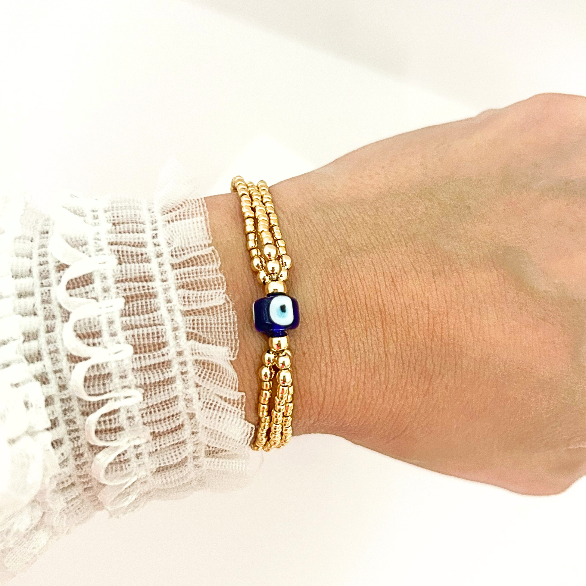 Minimalist evil eye bracelet with gold beads and a protective blue glass charm, perfect for stacking or wearing alone.