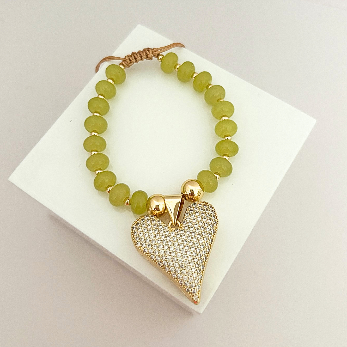 Adjustable bracelet with olive green matte beads, gold-tone details, and a pavé crystal heart pendant for an elegant statement.