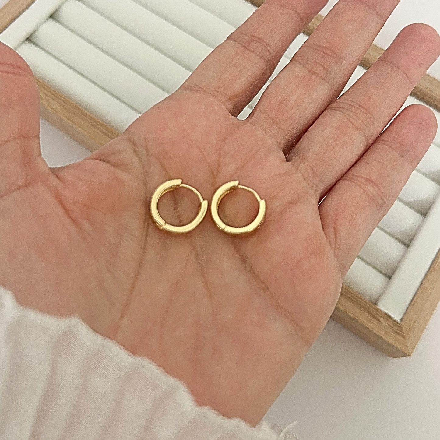 Pair of chunky gold huggie hoop earrings with CZ heart held in open palm