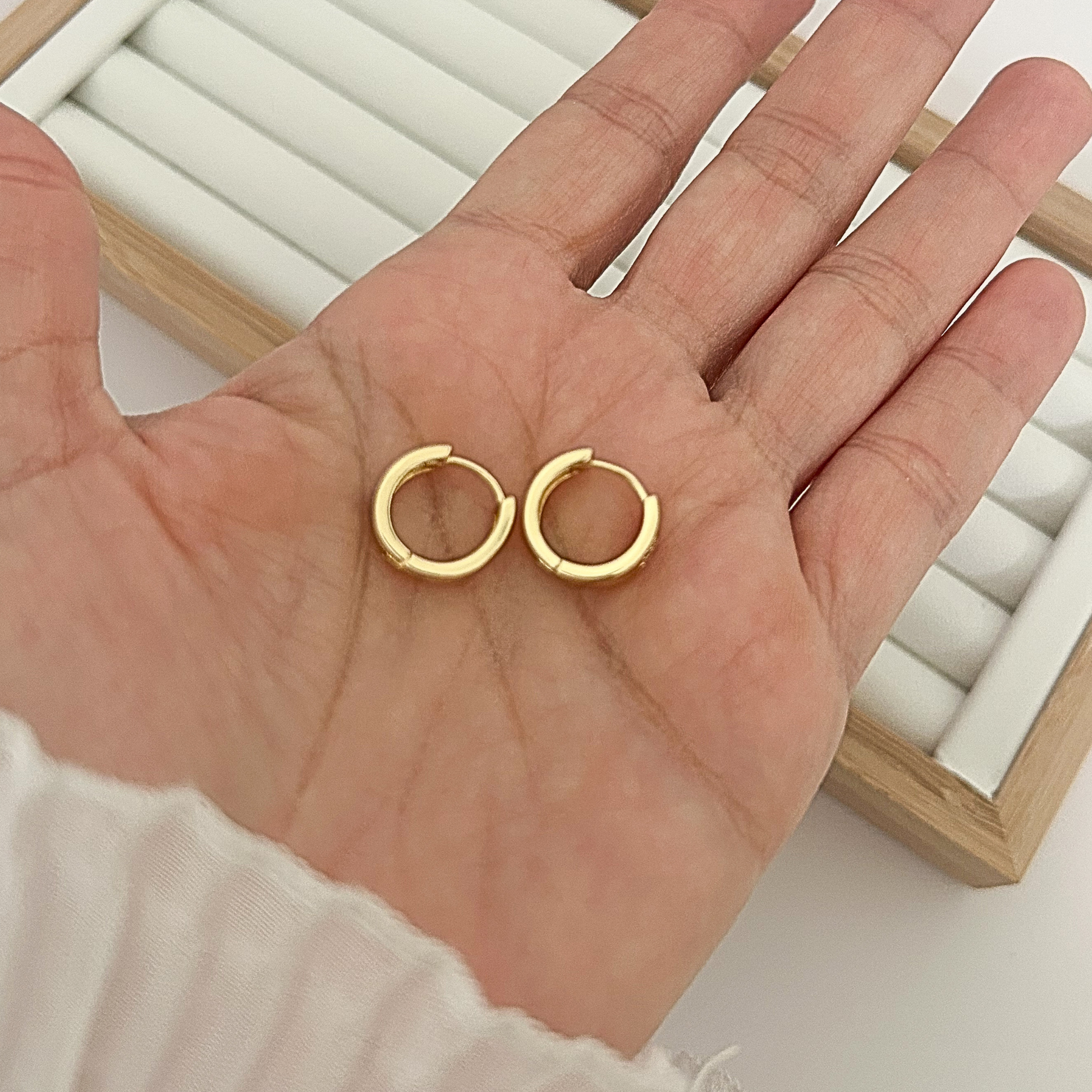 Pair of chunky gold huggie hoop earrings with CZ heart held in open palm