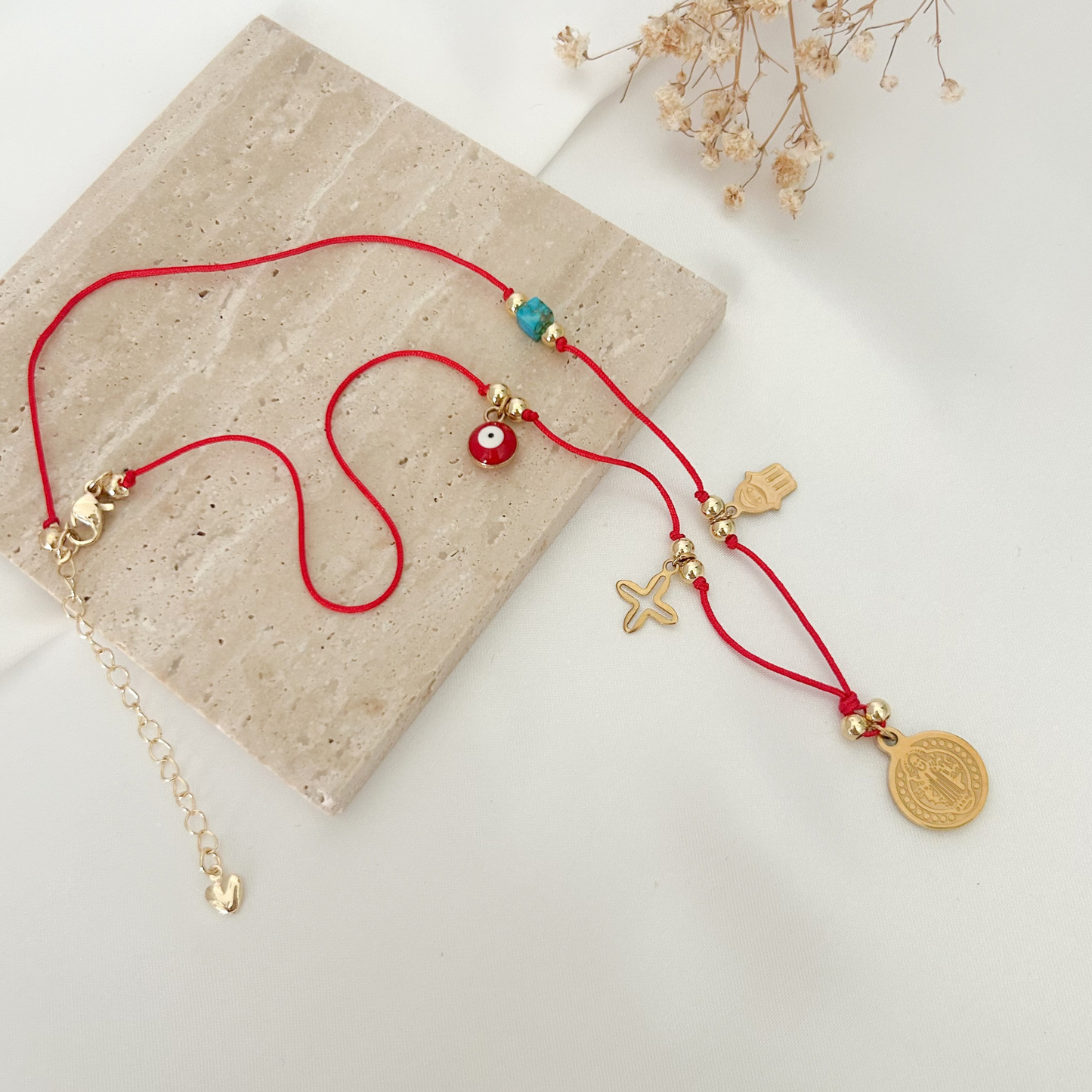 Protective red cord necklace with an evil eye charm, turquoise bead, Hamsa hand, starfish charm, and Saint Benedict medal in a gold-tone finish.