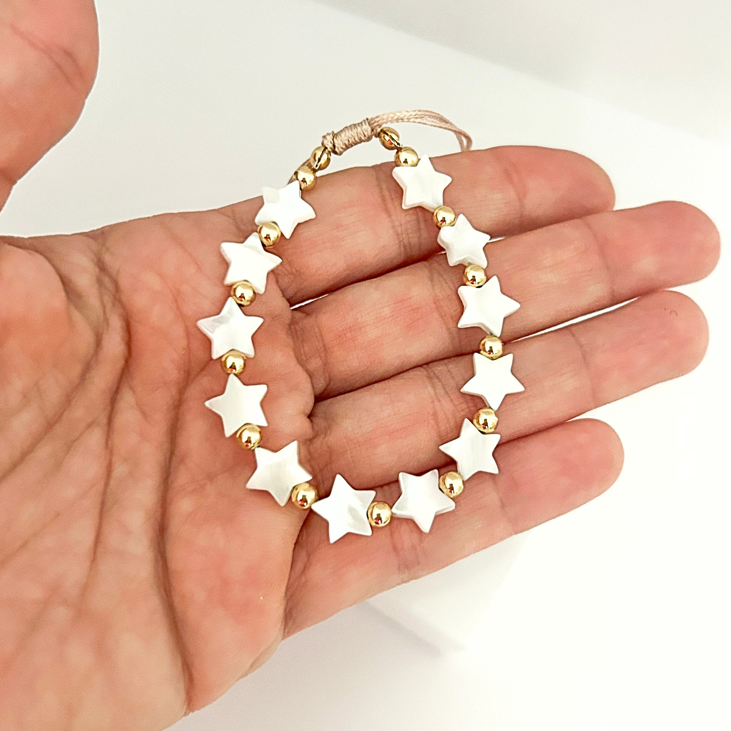 Handmade adjustable bracelet with white star beads and gold-tone spacers, offering a timeless and charming look.